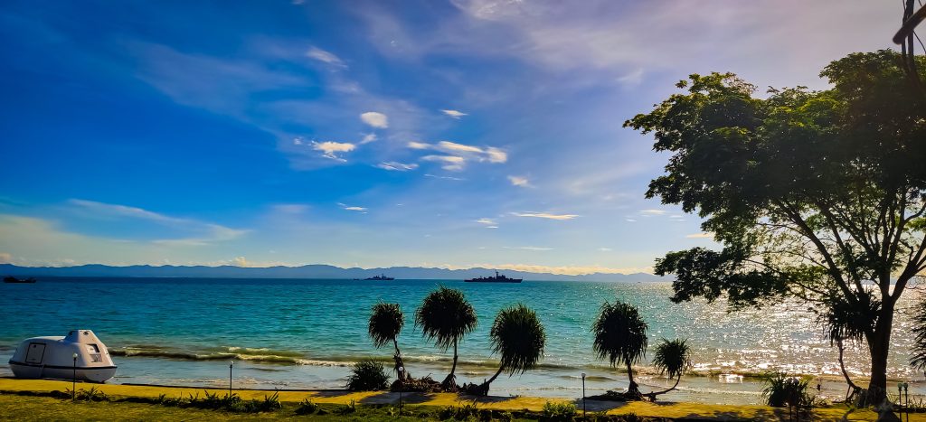 Turquoise water and sandy beach at Saint Martin's Island, Bangladesh, with a lifeboat and trees in the foreground.