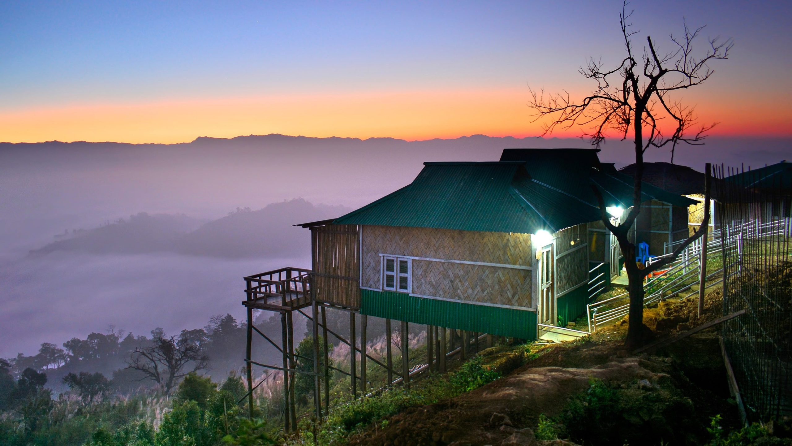 Scenic view of a resort cottage at Sajek Valley perched on a hilltop with foggy mountains in the background
